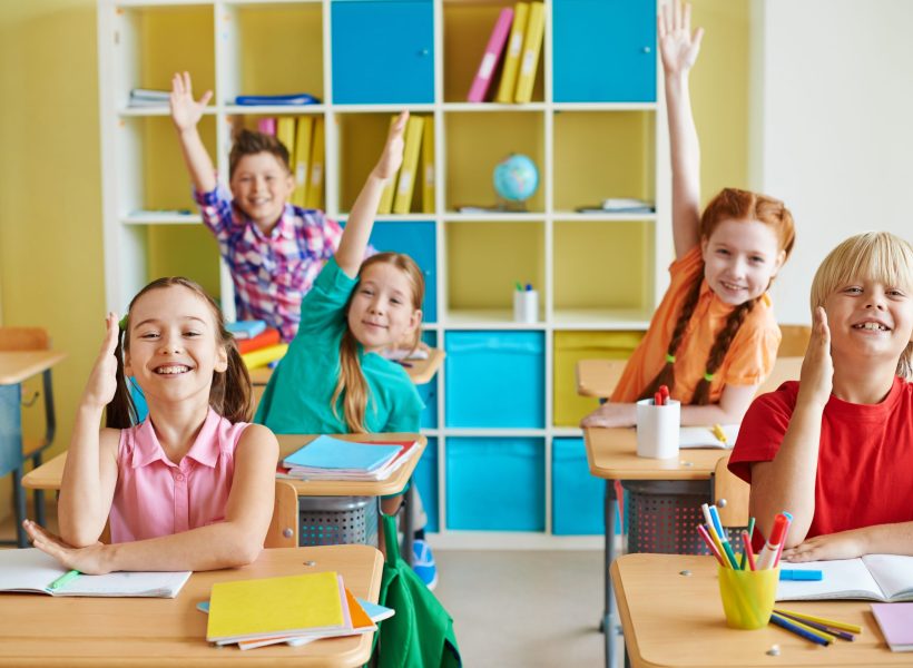 Happy classmates raising hands at lesson